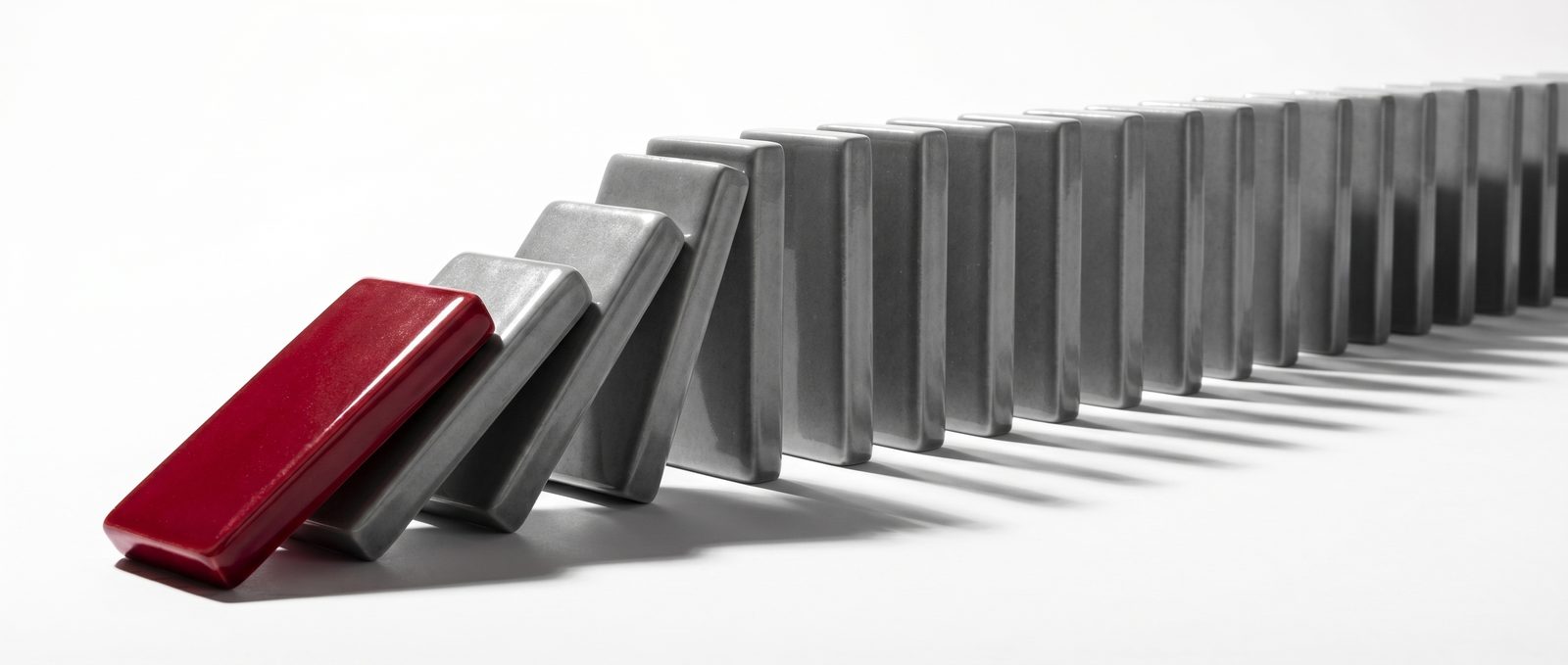 A row of dominoes mid-cascade, with a single red domino tipping the rest into a falling line